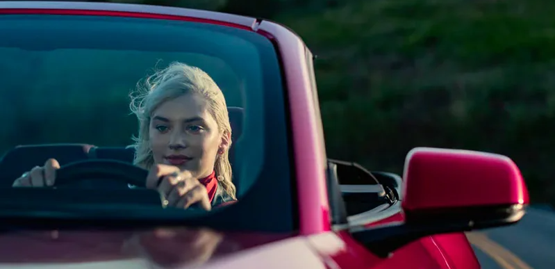 A closeup of the drivers side of a red 2025 Ford Mustang with a blonde lady driving.
